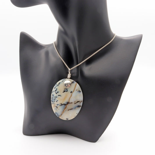 A truly magnificent Dendritic Agate pendant, meticulously handcut and polished in our USA studio. This exceptional cabochon pendant showcases striking black branching inclusions set against a background that transitions from opaque to partially translucent. The entire piece is gracefully encased in the shimmering embrace of Argentium® 935 Silver.