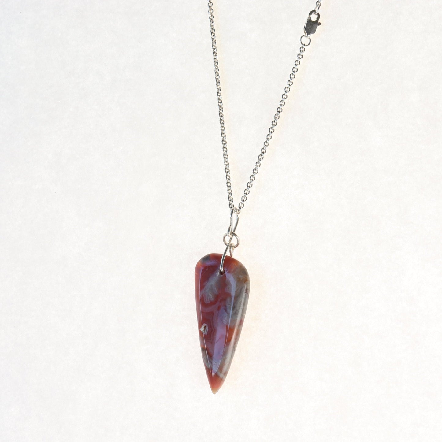  A Crazy Lace Agate arrow shaped gemstone pendant. 
Handcut and freeform polished on both sides to reveal the unique swirling patterns and vibrant mauve deep reds and gray hues. Wear with complementary chain included or with you own favorite necklace.