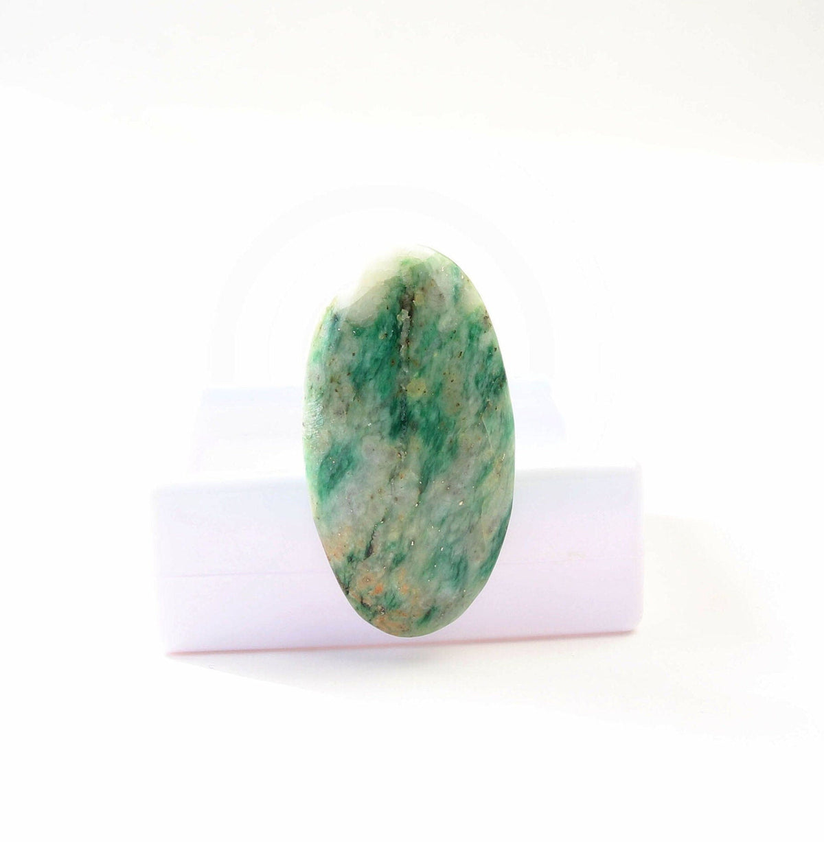Hand-cut Mariposite oval cabochon with green and creamy white natural pattern, standing against white gem box and displayed on a clean white background.