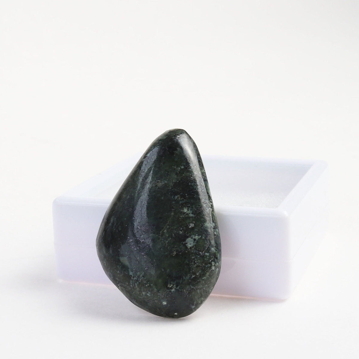 Natural freeform Moss Agate cabochon with mottled green pattern standing against white gem box shown on white background.