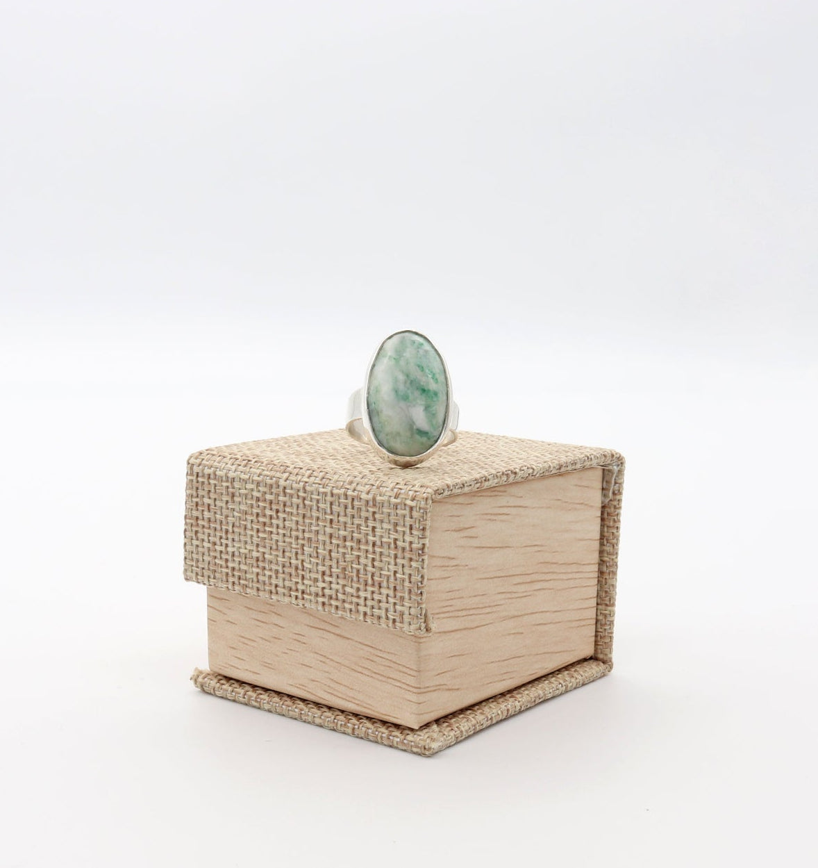 An Argentium silver Mariposite oval ring on a small light canvas wood gift box, photographed against a seamless white background.