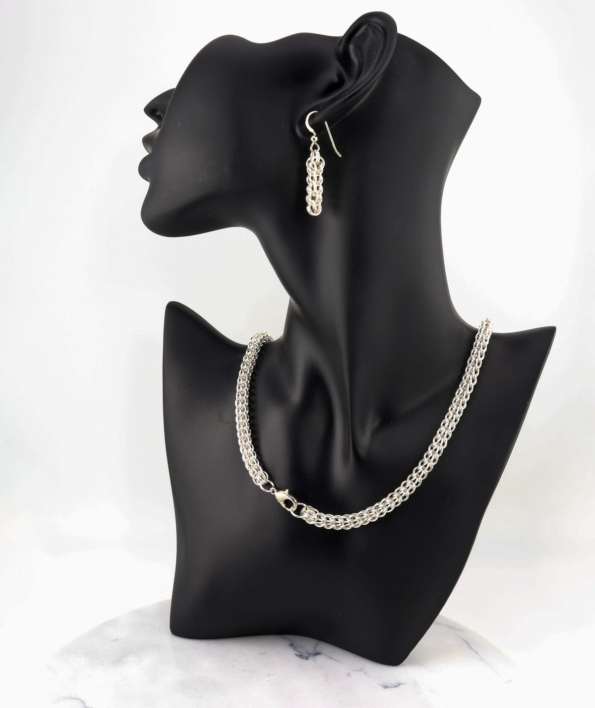 An Argentium silver persian weave chain necklace and matching drop earring displayed on a black mannequin bust against a white background.