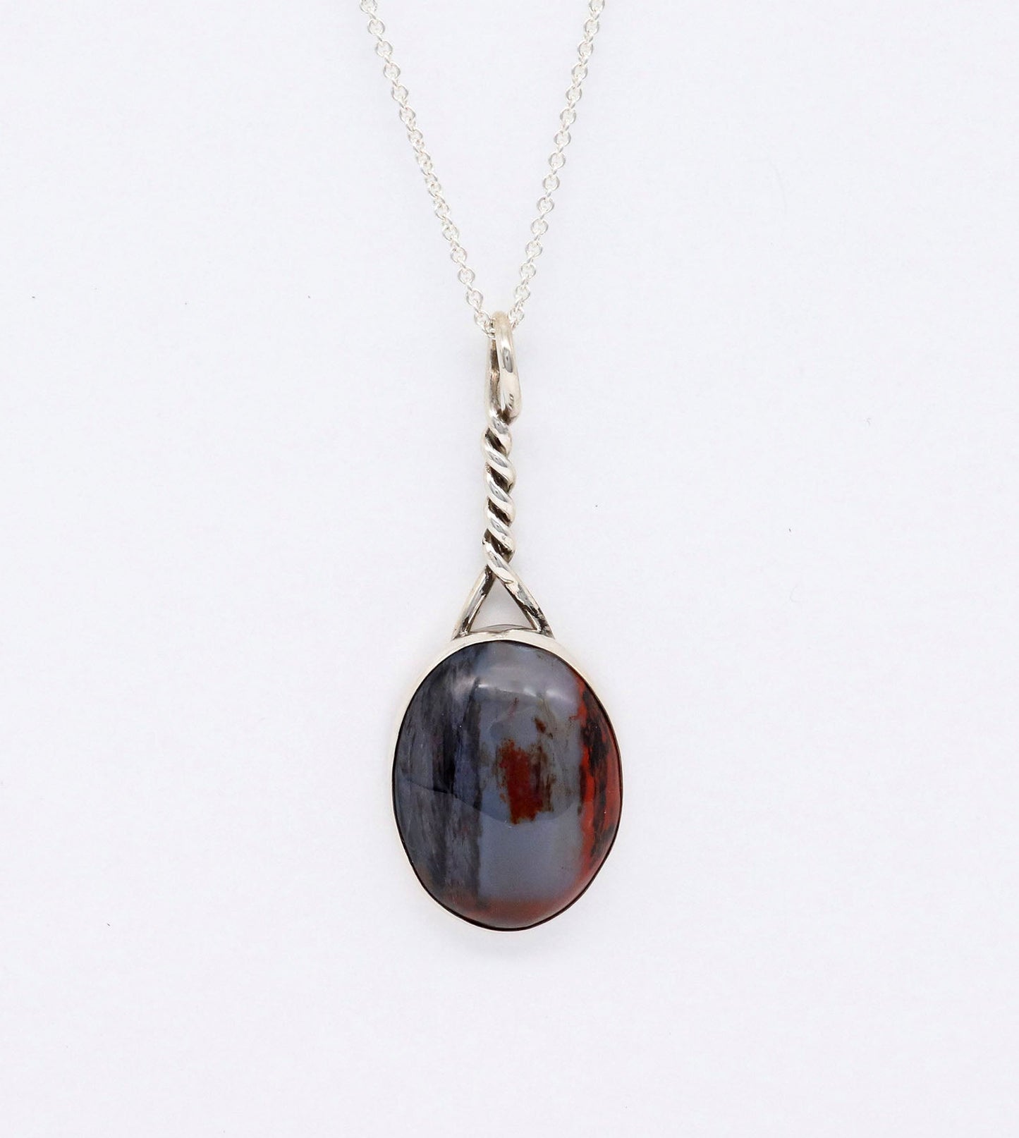 Oval shaped natural Petrified Rainbow Wood pendant set in solid Argentium silver bezel with custom twist bail.  Shown suspended from Argentium silver chain on light gray background.