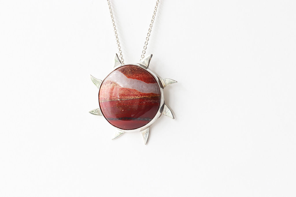 Snakeskin Jasper pendant, hand-cut and polished to showcase its vibrant flaming red, rich brown, and creamy natural patterns. Encased in premium Argentium® 935 silver shown on white background suspended from Argentium necklace chain.