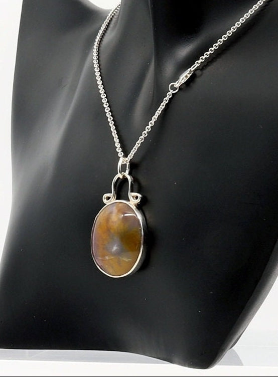 A Petrified Rainbow Wood pendant shown on black resin jewelry mannequin  with Argentium silver necklace chain with lobster clasp and shown against white background.