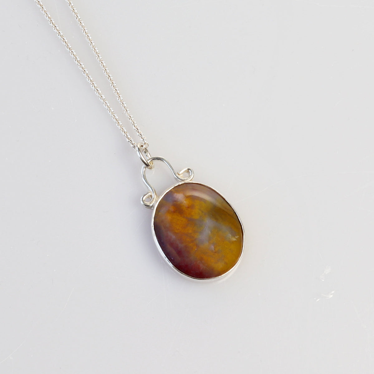 A silver necklace with an oval Petrified Wood pendant featuring a marbled brown, amber, and reddish-orange stone, displayed on a clean white background.