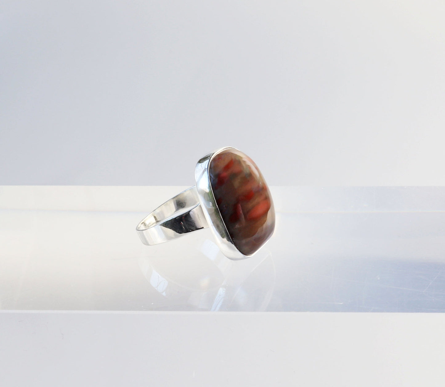 A Petrified Rainbow Wood men's gemstone ring.  This gemstone has been handcut and polished in our Missouri studio to showcase the natural red and brown hues and captivating patterns.  Encased in sterling 935 Argentium silver with a fine silver bezel (.999) which work together to create a bold and timeless eye-catching design.  