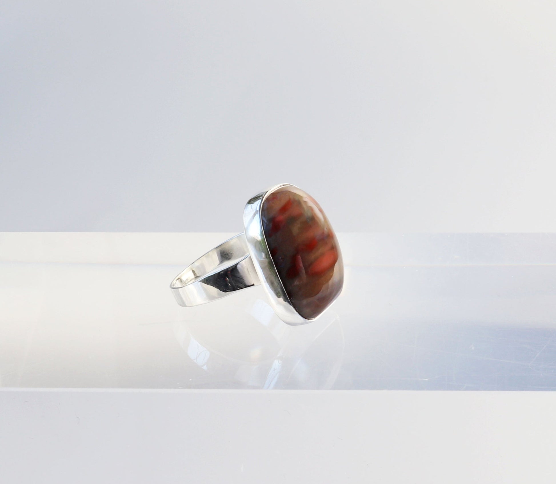 A Petrified Rainbow Wood men's gemstone ring.  This gemstone has been handcut and polished in our Missouri studio to showcase the natural red and brown hues and captivating patterns.  Encased in sterling 935 Argentium silver with a fine silver bezel (.999) which work together to create a bold and timeless eye-catching design.  