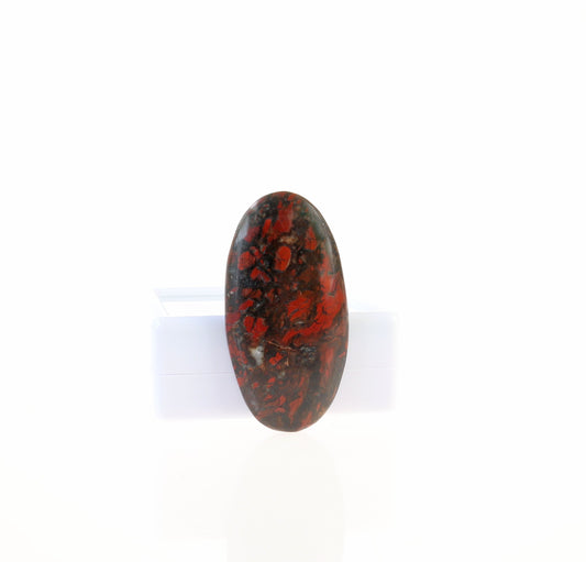 Natural Red and Black jasper cabochon, hand-cut and polished into an oval shape shown on white background against white gem box.