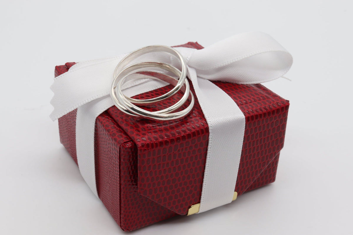 Handcrafted solid sterling silver rolling ring with three interlocking polished bands displayed on top of a textured red gift box wrapped with a white ribbon and bow, set against a plain white background.