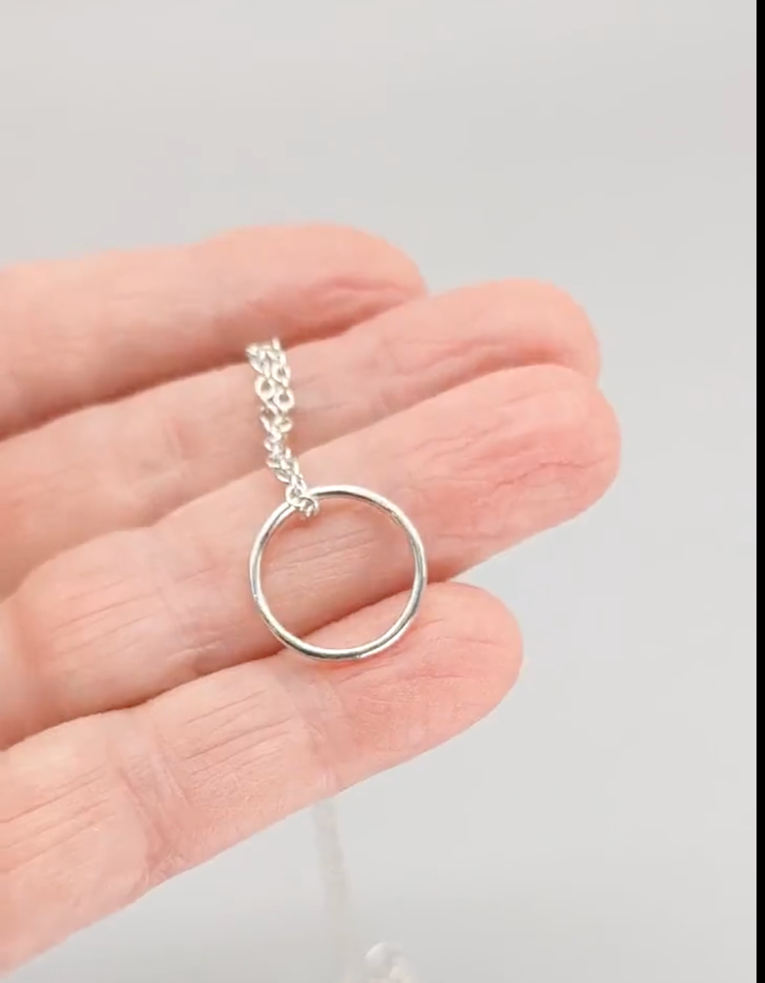 Silver ring necklace on a hand against a light gray background