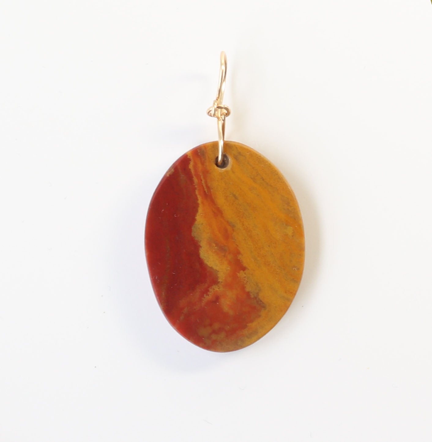 A Sonoran Sunrise Pendant. Hand-cut and polished to reveal the vivid bands of deep red cuprite swirls along with golden ochre and sun-baked mustard tones. Finished with a custom infinity bow bail in 14/20 gold-filled wire. Shown on white background.