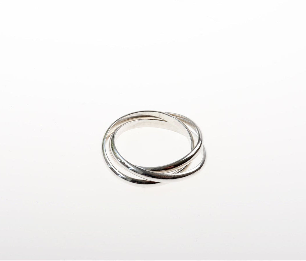 Handcrafted solid sterling silver rolling ring with three interlocking polished bands on white cushion on white background.