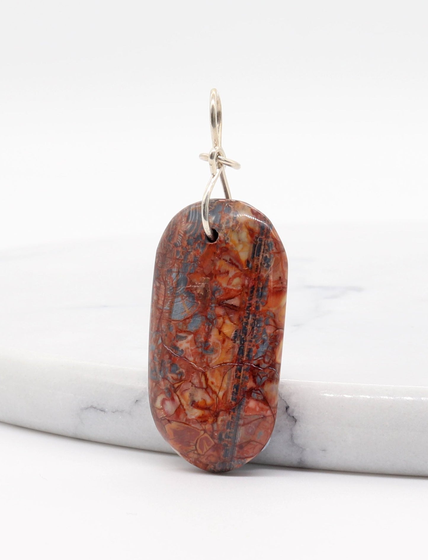 A Stony Creek Jasper gemstone pendant. Handcut and polished on both sides to showcase thered and blue patterns of the stone. The pendant is designed with an original infinity bow shaped wire bail made from Argentium® 935 Silver 