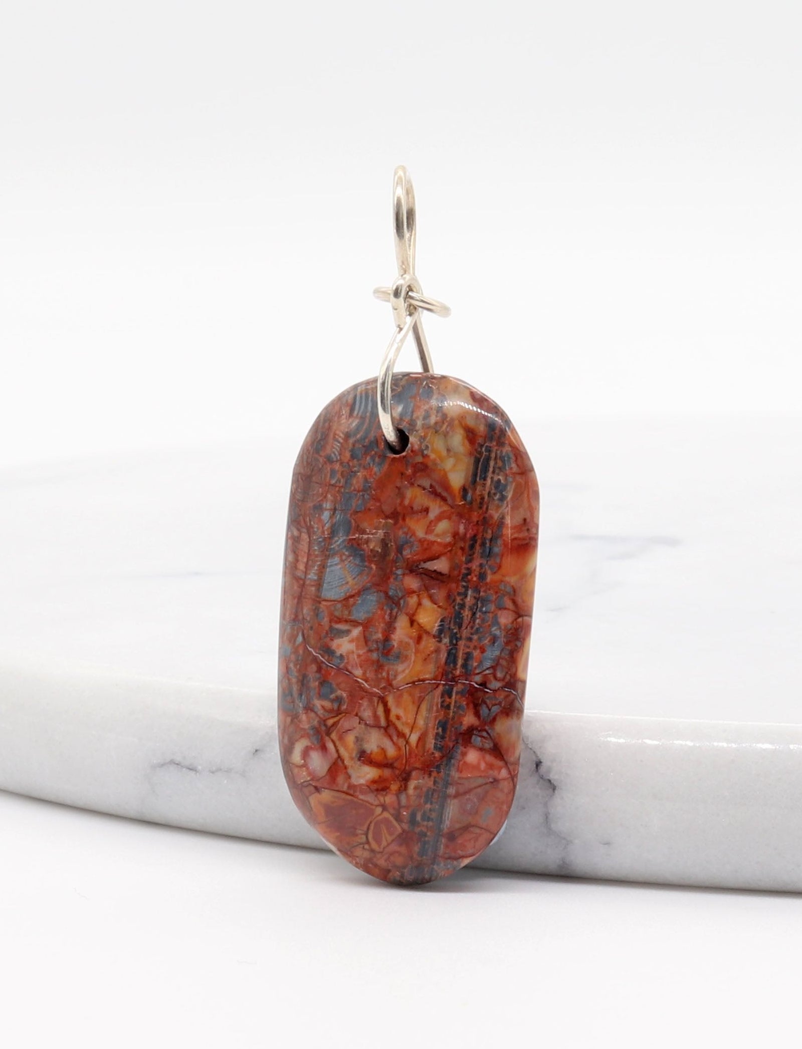 A Stony Creek Jasper gemstone pendant. Handcut and polished on both sides to showcase thered and blue patterns of the stone. The pendant is designed with an original infinity bow shaped wire bail made from Argentium® 935 Silver 