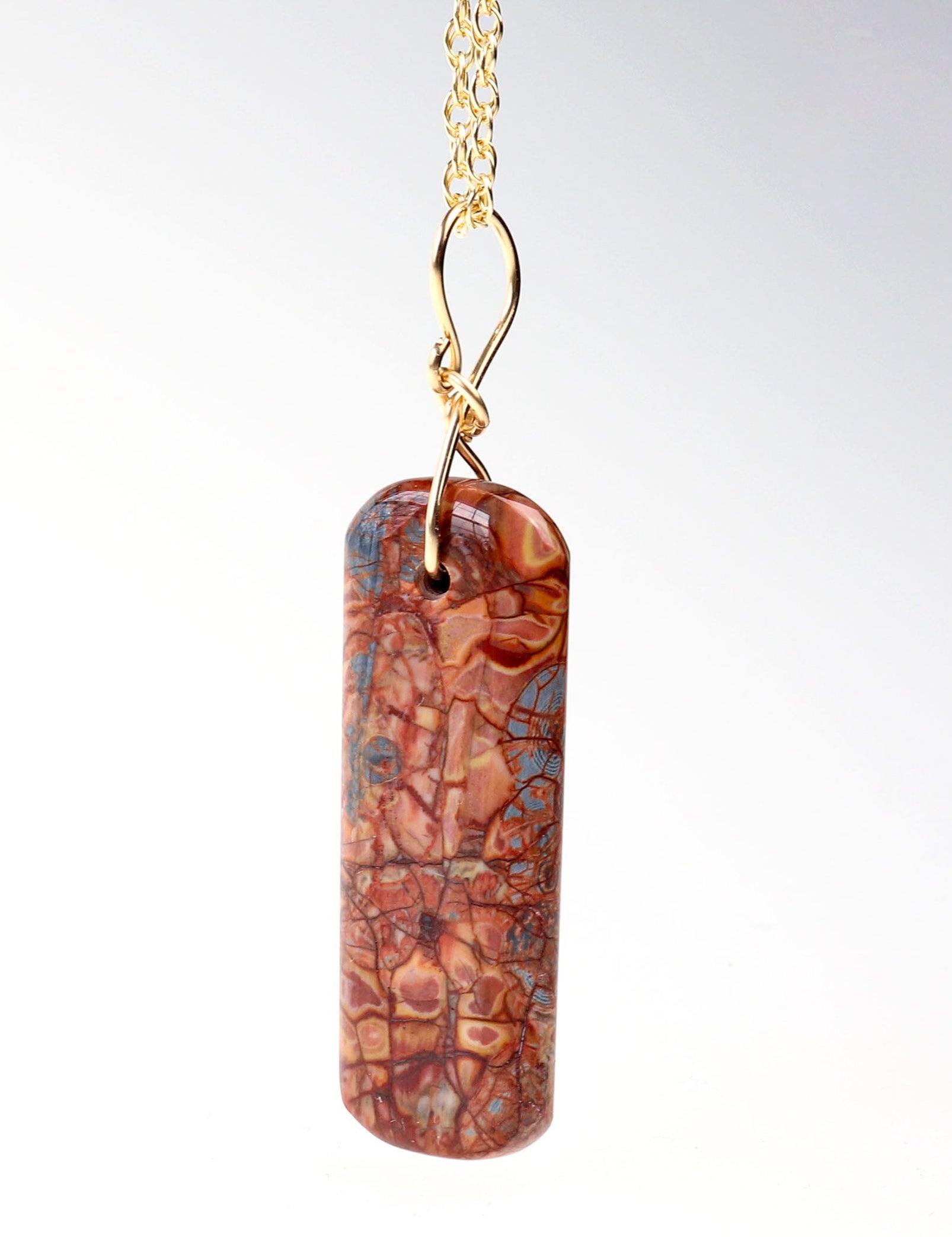 Stony Creek Jasper pendant  hand-cut and polished features bold red and deep blue patterns suspended from a handcrafted 14/20 Yellow Gold-Filled Infinity Bow Bail with optional Gold-Filled Rope chain against light gray background.