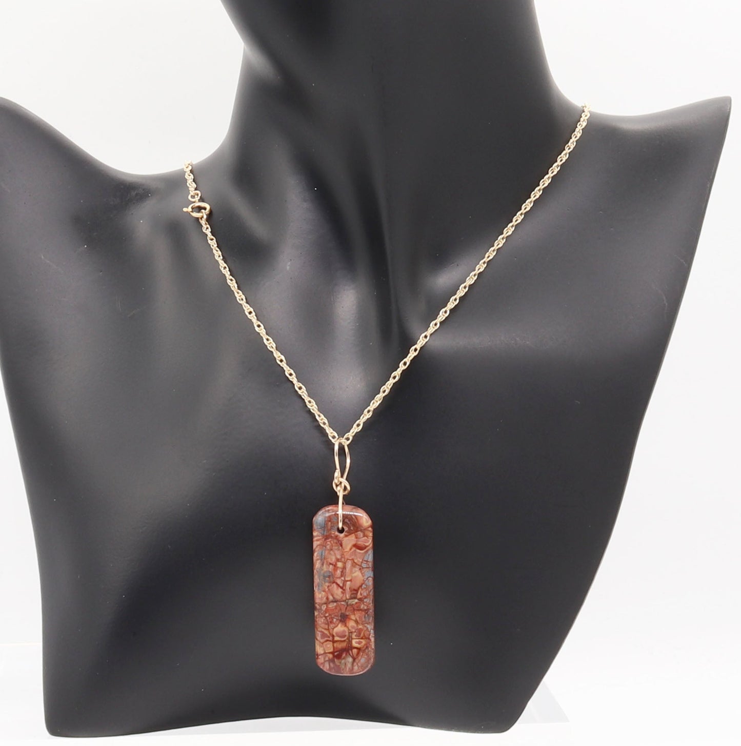 Stony Creek Jasper pendant  hand-cut and polished features bold red and deep blue patterns suspended from a handcrafted 14/20 Yellow Gold-Filled Infinity Bow Bail with optional Gold-Filled Rope chain on black resin jewelry form against white background.