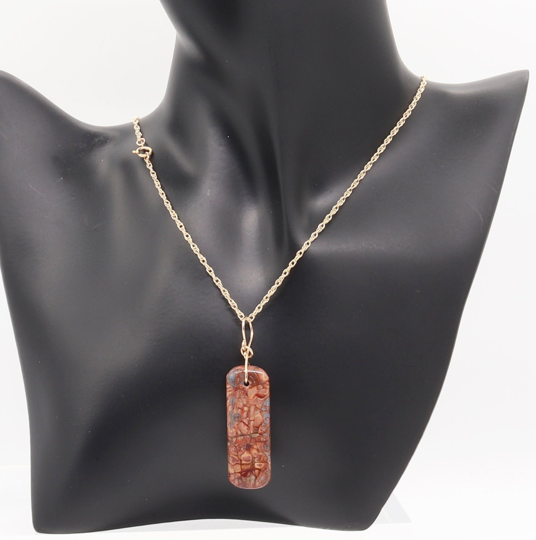 Stony Creek Jasper pendant  hand-cut and polished features bold red and deep blue patterns suspended from a handcrafted 14/20 Yellow Gold-Filled Infinity Bow Bail with optional Gold-Filled Rope chain on black resin jewelry form against white background.