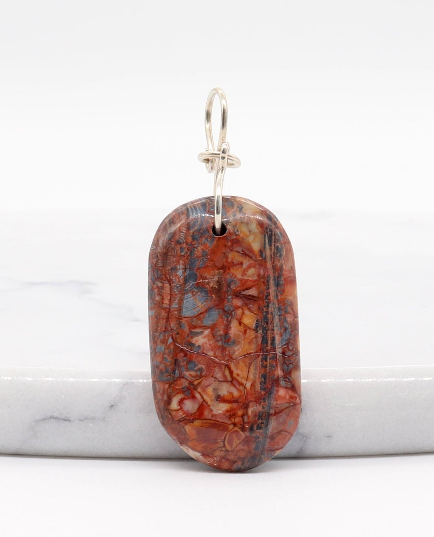 A Stony Creek Jasper gemstone pendant. Handcut and polished on both sides to showcase the unique red and blue patterns of the stone. &nbsp;The pendant is designed with an original infinity bow shaped wire bail made from Argentium® 935 Silver that is tarnish resistance and has a remarkable shine. &nbsp;To complete the look a complementary 935 Argentium® silver chain is included.