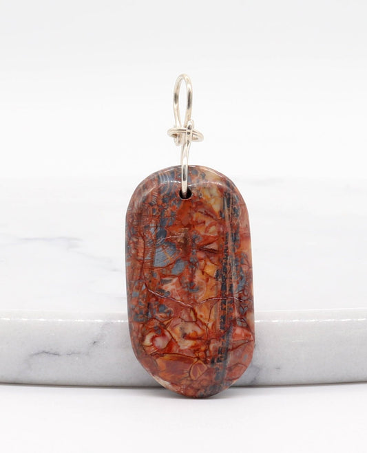 A Stony Creek Jasper gemstone pendant. Handcut and polished on both sides to showcase the unique red and blue patterns of the stone. &nbsp;The pendant is designed with an original infinity bow shaped wire bail made from Argentium® 935 Silver that is tarnish resistance and has a remarkable shine. &nbsp;To complete the look a complementary 935 Argentium® silver chain is included.