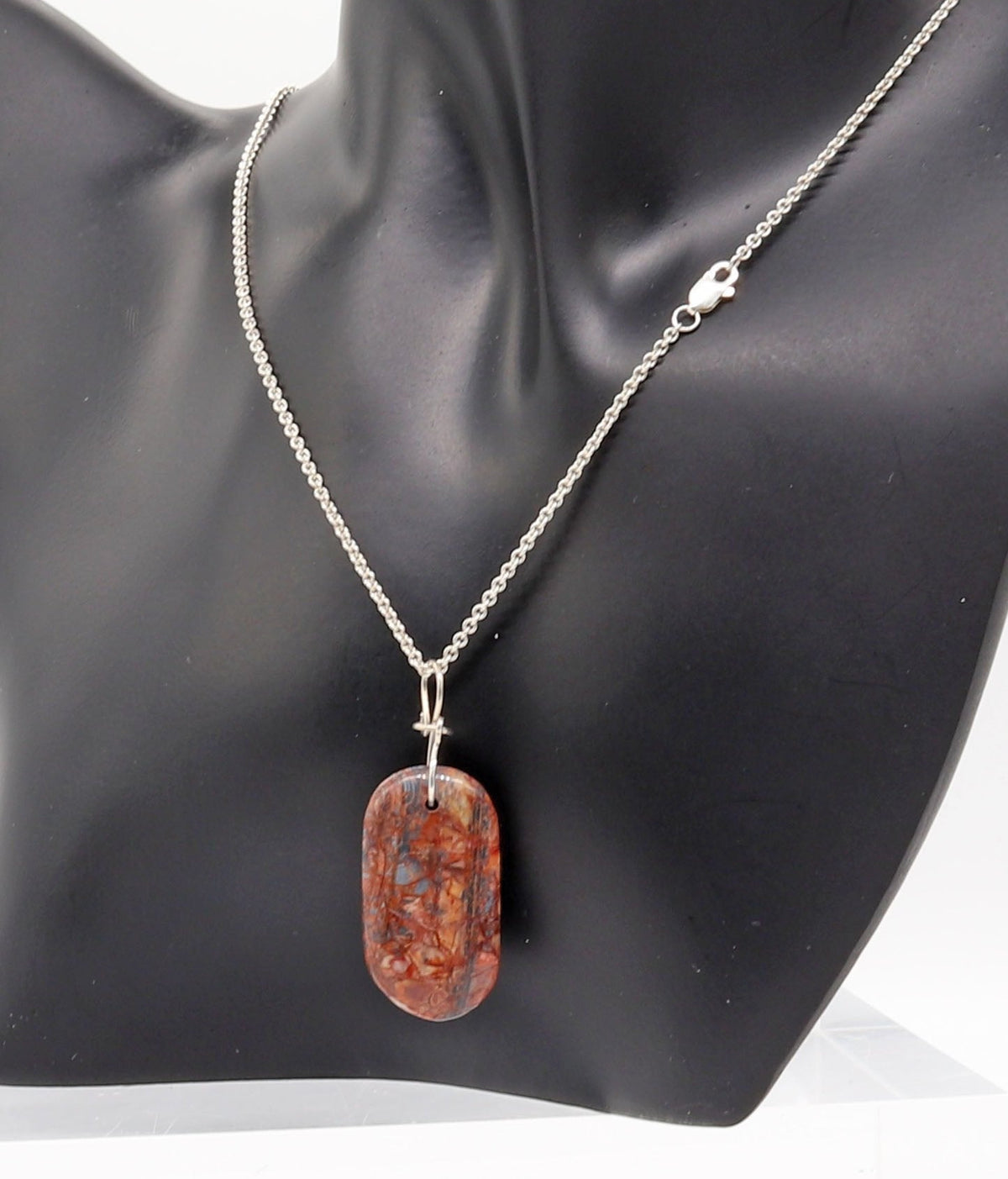 A Stony Creek Jasper gemstone pendant. Handcut and polished on both sides to showcase the unique red and blue patterns of the stone.  Shown on a black resin jewelry form against a white background.