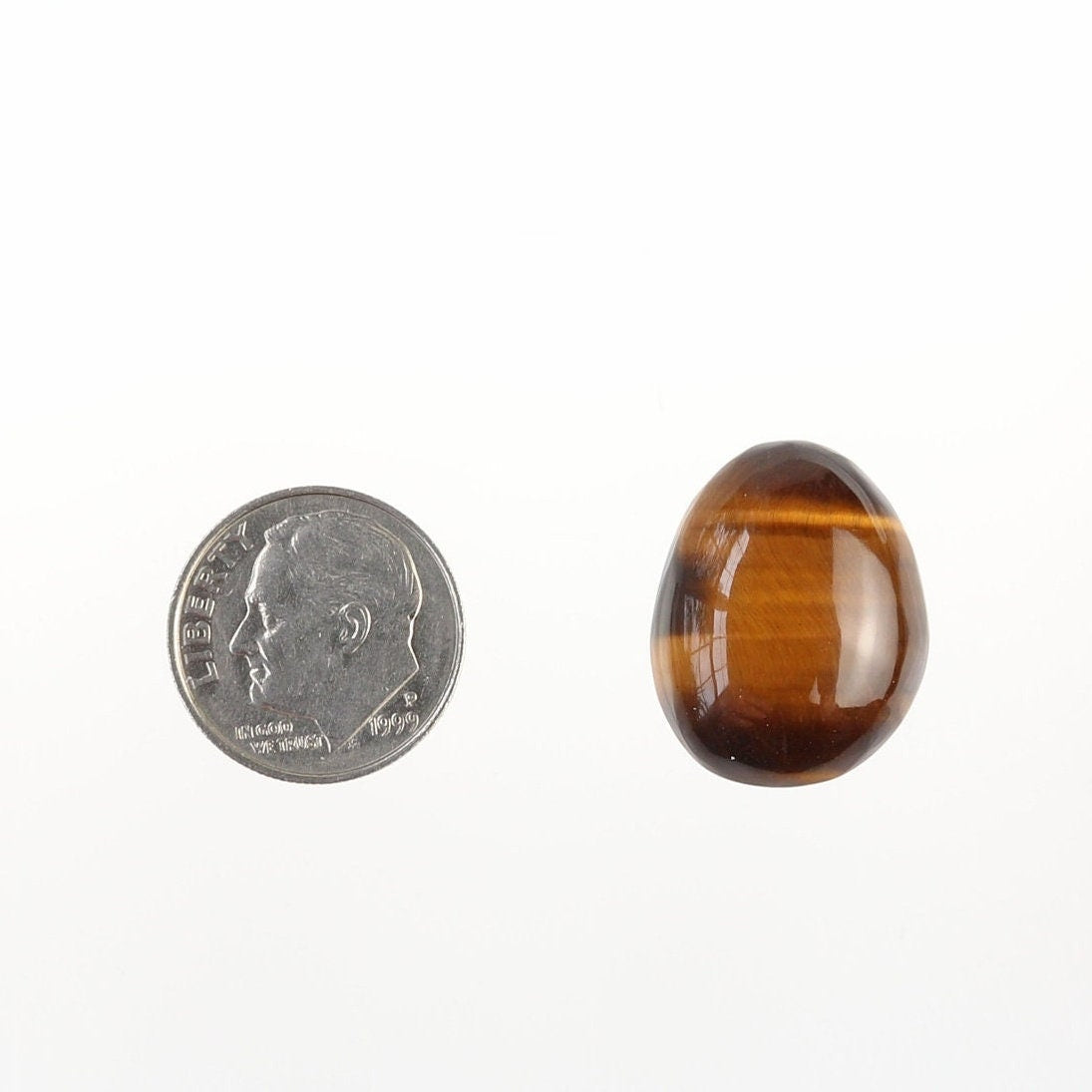 Natural Tiger's Eye cabochon shown beside a U.S. dime for size comparison, displaying golden-brown banding and chatoyancy.