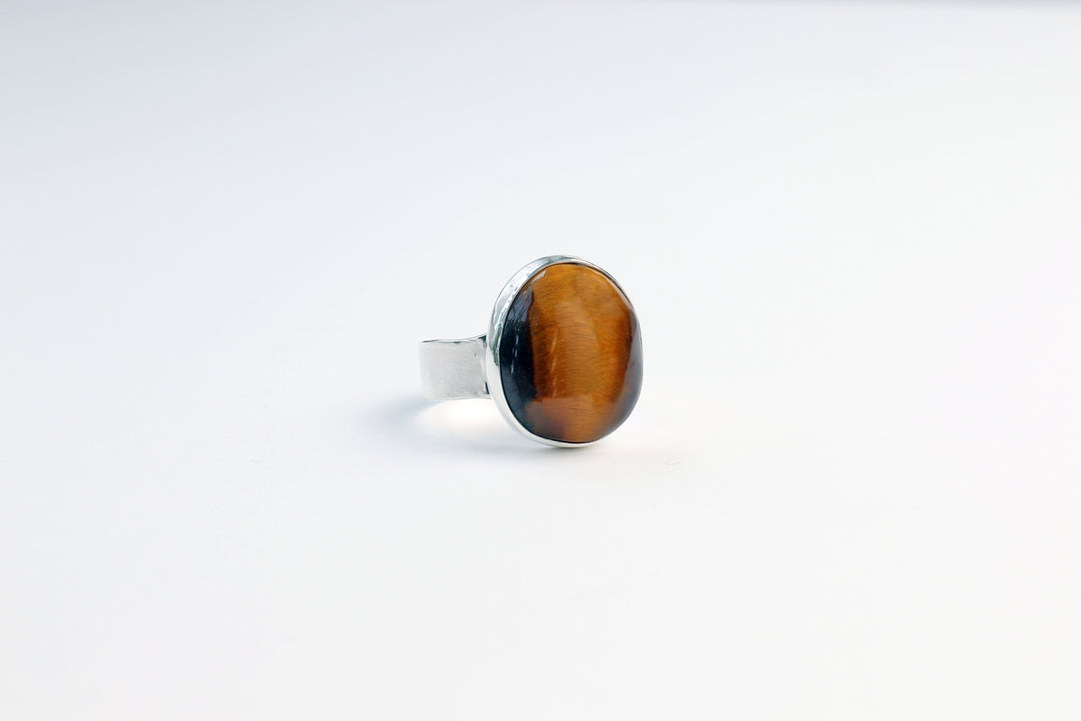 Left angle of a Natural Tiger's Eye ring in solid Argentium 935 silver, handcrafted by Elkhorn Silver, shown on light gray background.