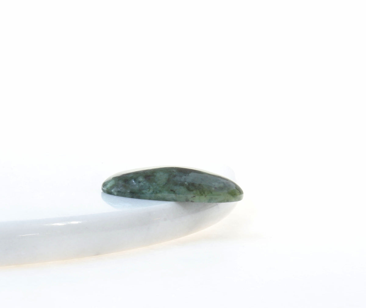 A side angle of a polished Wyoming Jade stone cabochon against a white marble slab, photographed on a clean light gray background.