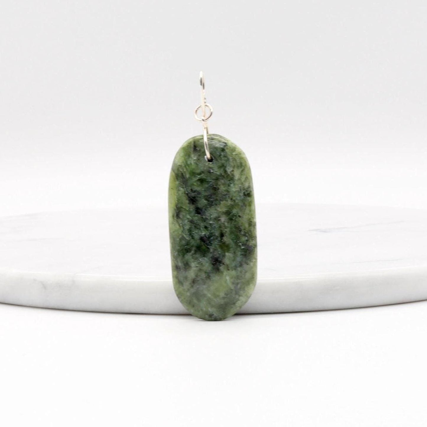 Wyoming Jade Pendant with Argentium Silver Custom bow shaped bail shown leaning on a whiite marble slab against a white background.