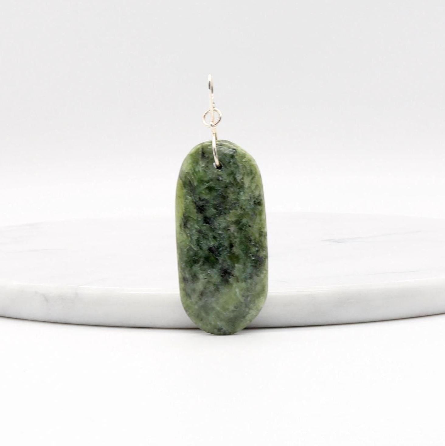 Wyoming Jade Pendant with Argentium Silver Custom bow shaped bail shown leaning on a whiite marble slab against a white background.