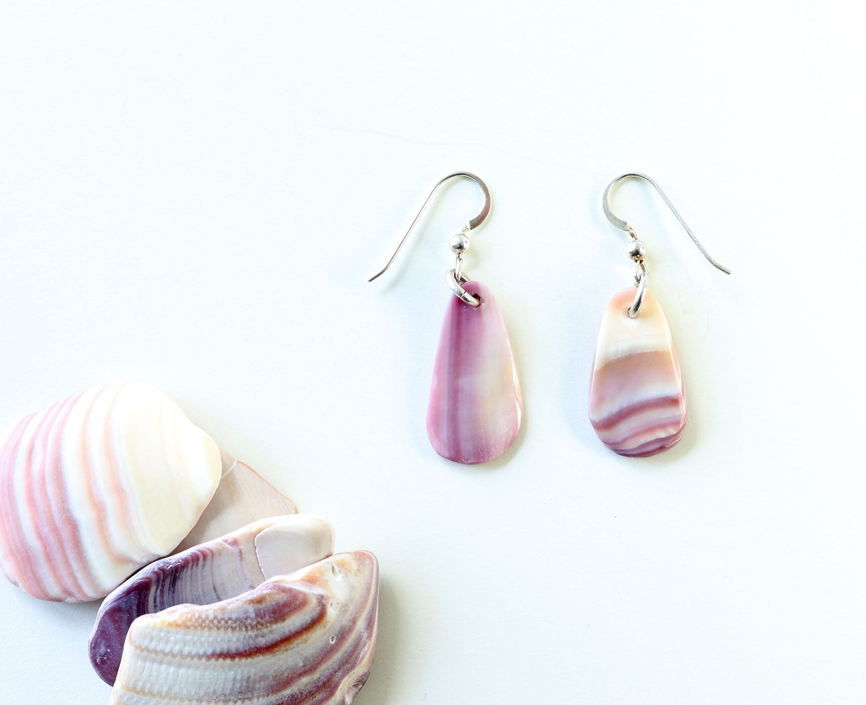 Reversible with unique patterns on both sides shown next to raw Quahog shells — one-of-a-kind shell earrings handcrafted in our Missouri studio using natural Quahog shells—known for soft lavender and cream tones. 