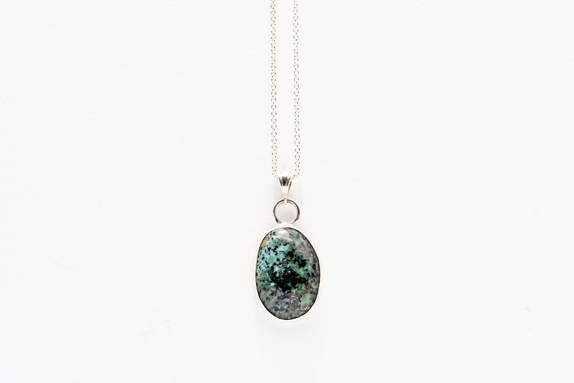 Fraser River Turquoise featuring blue green and black patterns showcased in Argentium Silver and fine silver setting. pendant on a white background