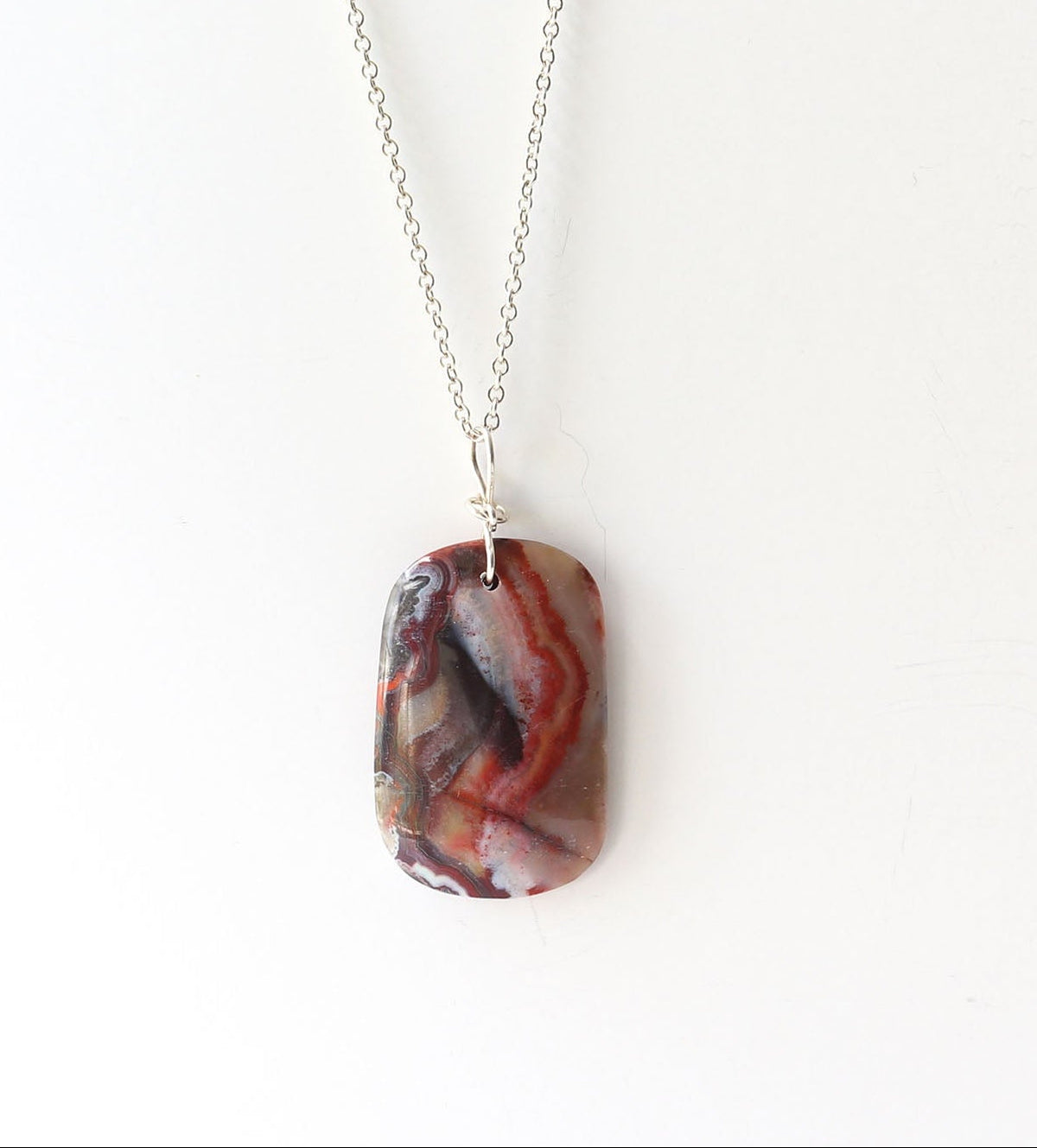 One-of-a-kind Red Mexican agate pendant, hand-cut and polished displays Deep red and black tones with natural Subtle translucency that catches the light Finished with a handcrafted infinity bow bail in 935 Argentium® Silver paired with Argentium necklace
Shown on white background .