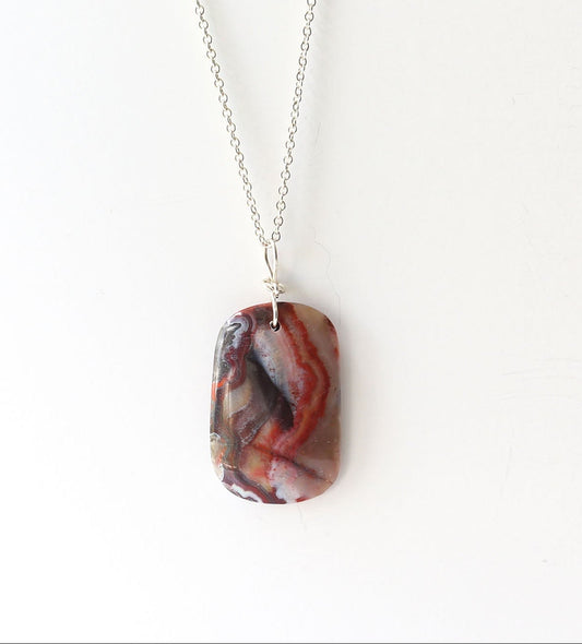 One-of-a-kind Red Mexican agate pendant, hand-cut and polished displays Deep red and black tones with natural Subtle translucency that catches the light Finished with a handcrafted infinity bow bail in 935 Argentium® Silver paired with Argentium necklace
Shown on white background .