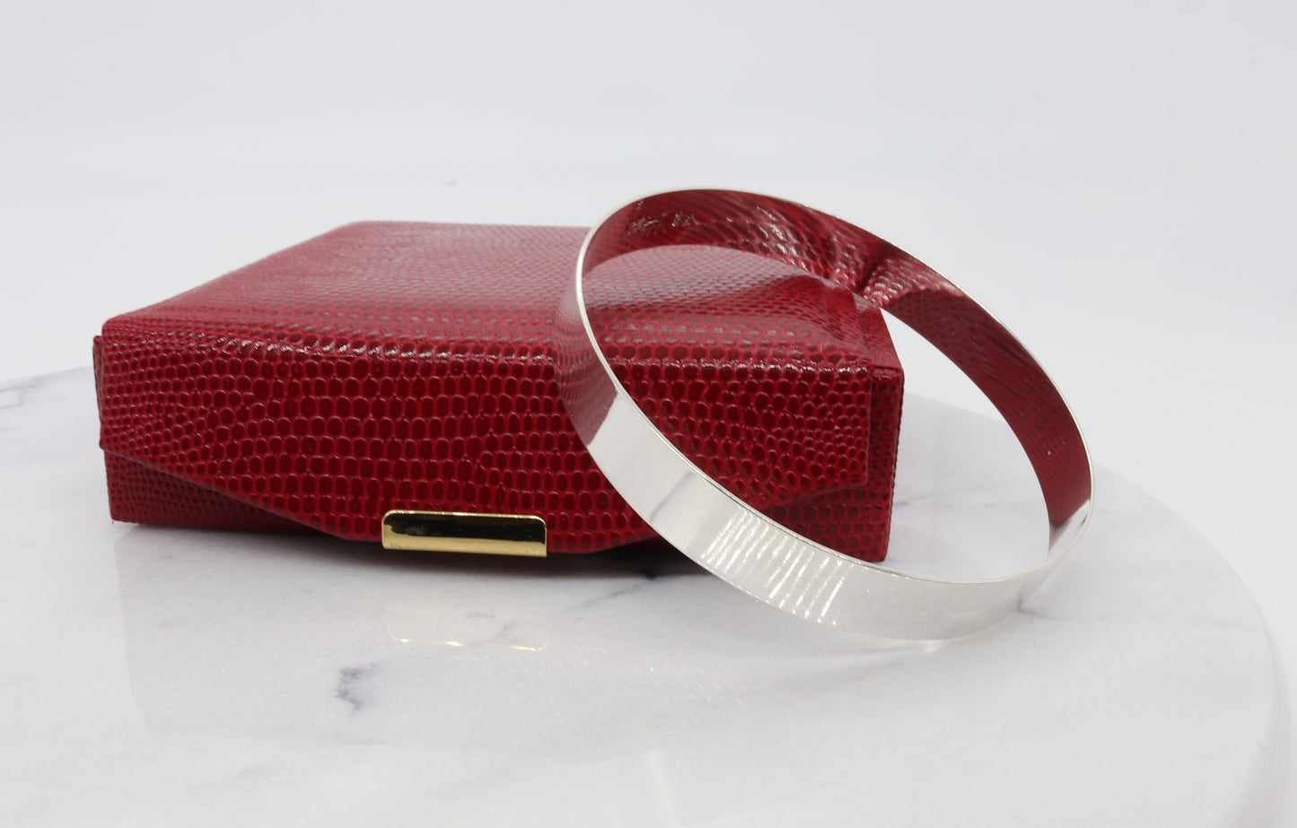 Argentium bracelet bangle shown next to red gift box against white marble background.
