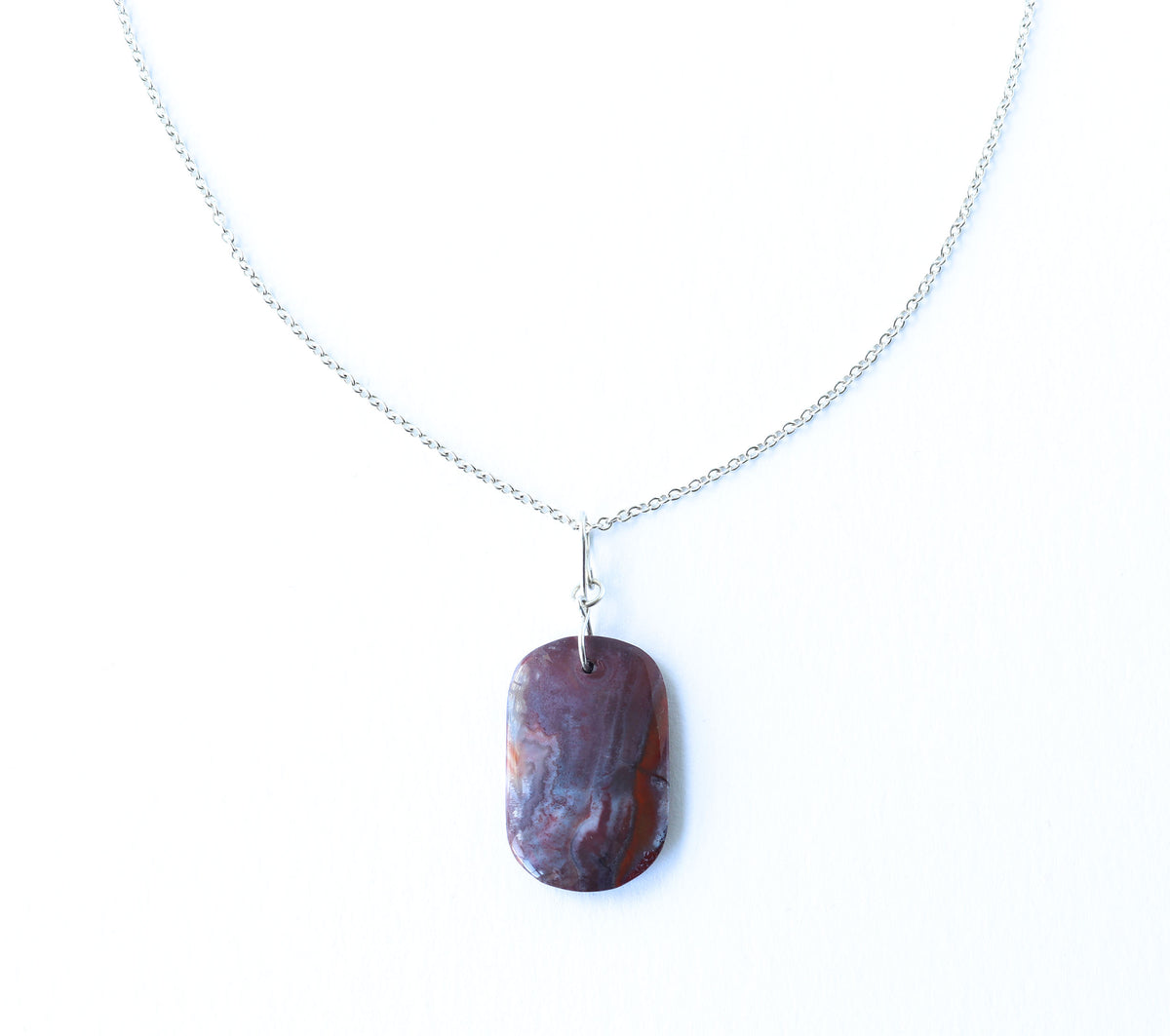 A Red Mexican Agate pendant features layered shades of warm red, burgundy, muted mauve, soft gray, and cream, with natural banding.  handcrafted infinity bow-style bail in solid Argentium® 935 Silver and paired with our handcrafted 1.9 mm Argentium® Silver chain necklace