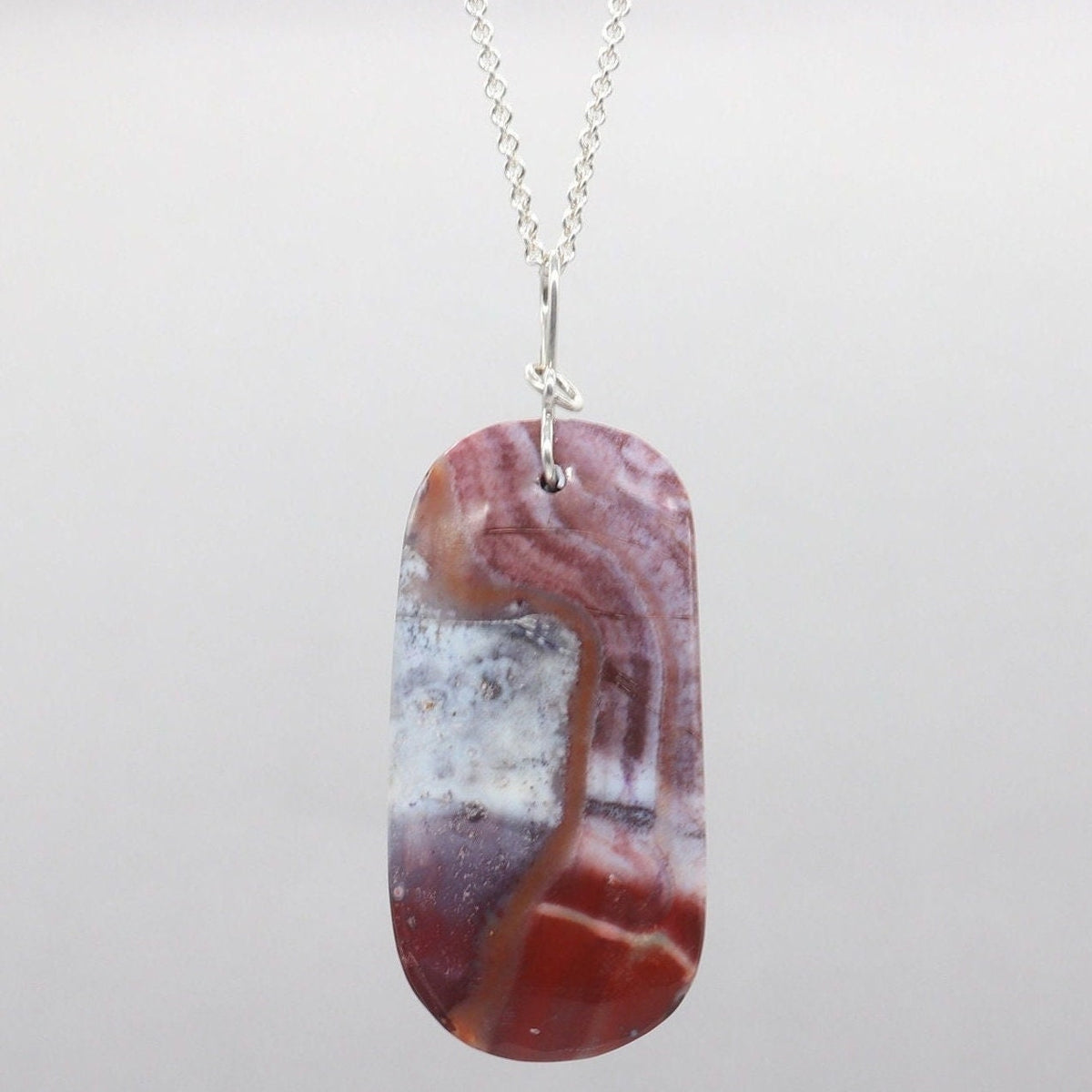 Red Mexican Agate pendant with Argentium Silver bail suspended from silver chain on white marble against gray background