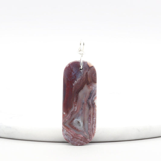 Front view of Red Mexico Agate pendant featuring soft lavender and mauve tones, polished to highlight translucent patterns, with a silver infinity-style bail.  Shown against white marble background.