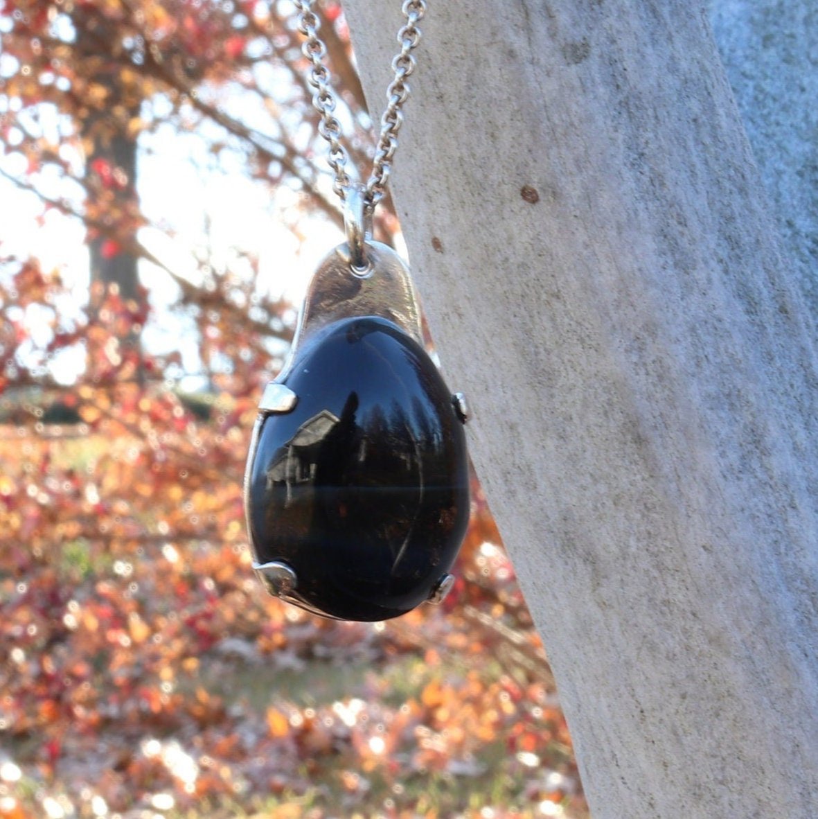 Natural Blue Tiger’s Eye pendant in Argentium 935 Silver with silver chain shown against branch with outside background.