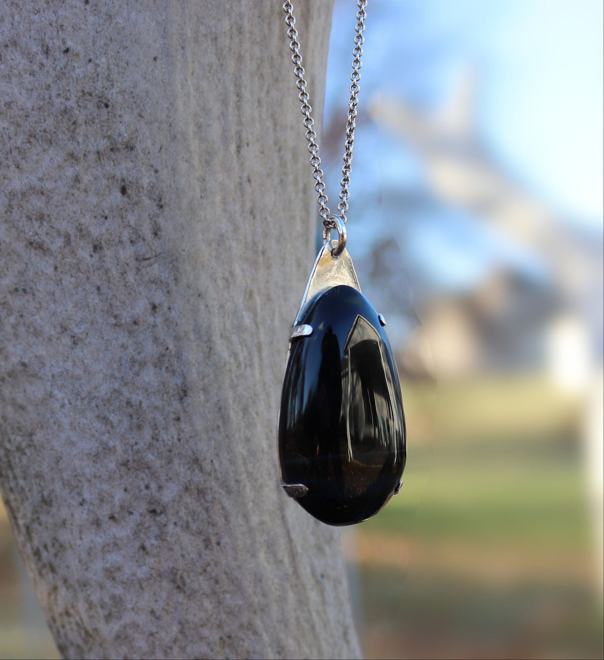 Handcrafted African Blue Tiger's Eye teardrop pendant with deep blue-black reflective gemstone, solid Argentium 935 silver tabbed setting and silver chain.  Shown against an elk branch in outdoor setting.