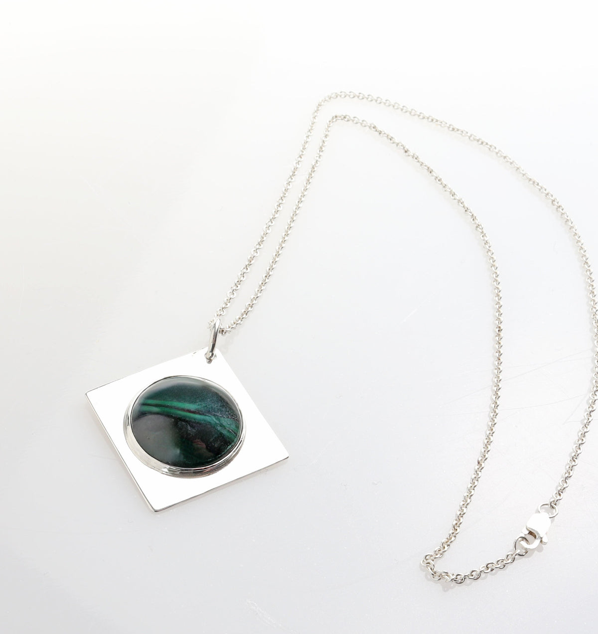 A silver necklace featuring a square pendant with a circular inset of dark green Malachite iridescent stone, displayed on a clean white background.