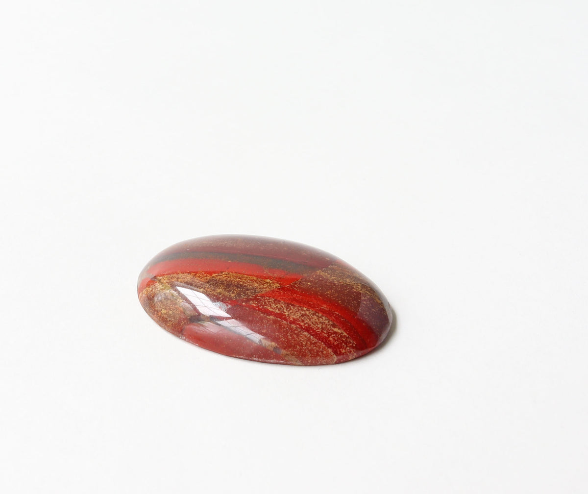 A polished oval Snakeskin Jasper cabochon with rich red and rust tones, accented by earthy brown, golden cream, and subtle gray areas set against a plain white background.