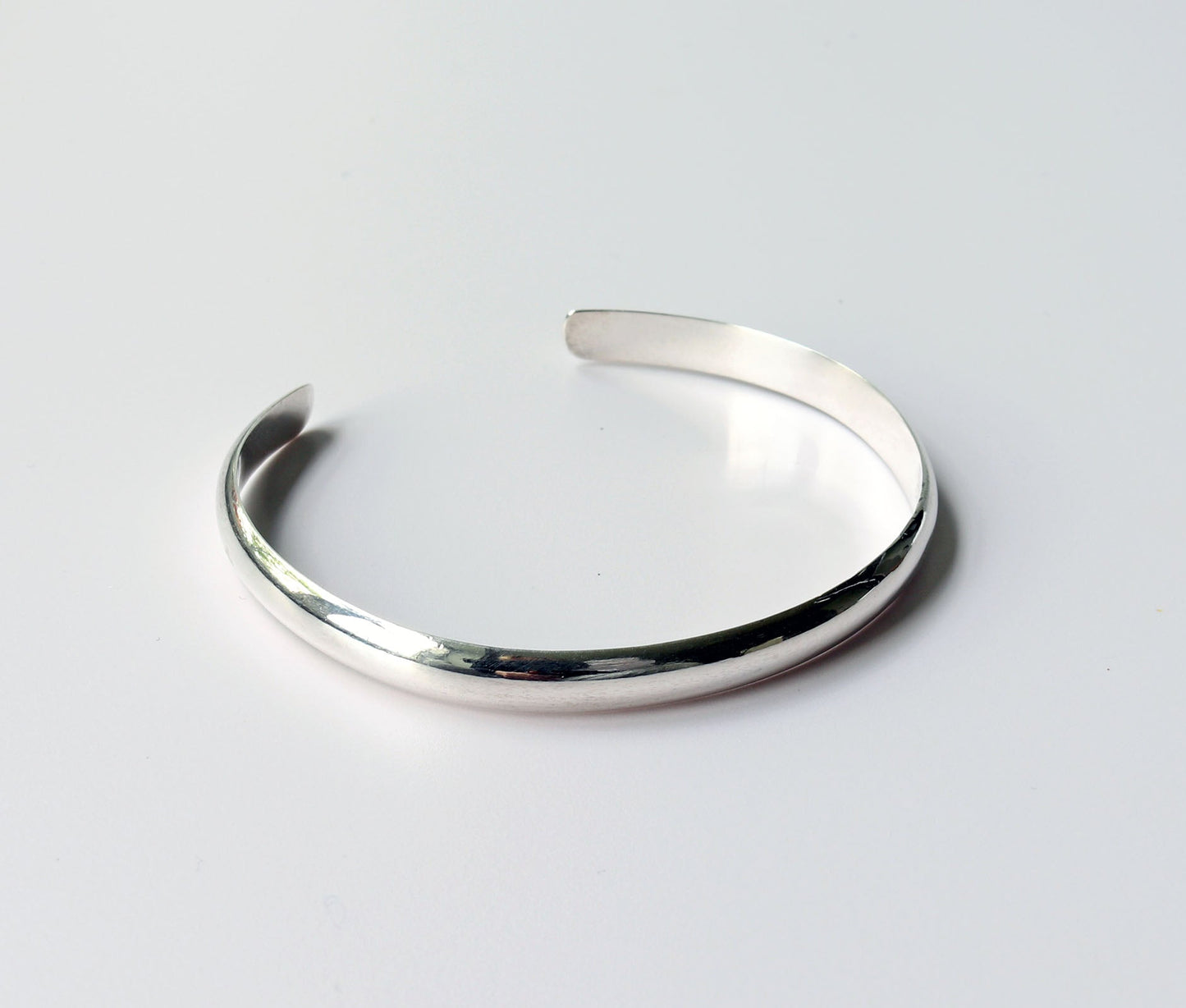 A Silver Cuff bracelet handcrafted in solid Argentium® 935. The gently curved low dome profile gives this cuff its sleek, modern look, while the open design allows for slight adjustability shown on light gray background.