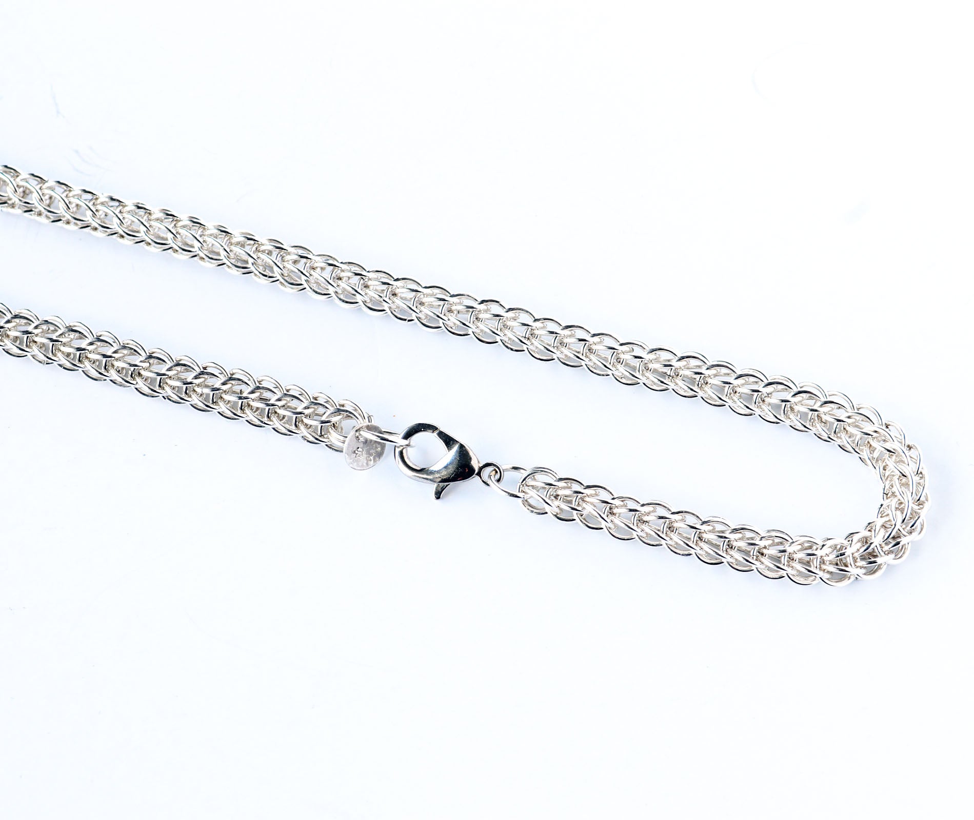 Closeup of teardrop lobster clasp and 6 and 1 Persian weave necklace.  Silver chain necklace on a white background