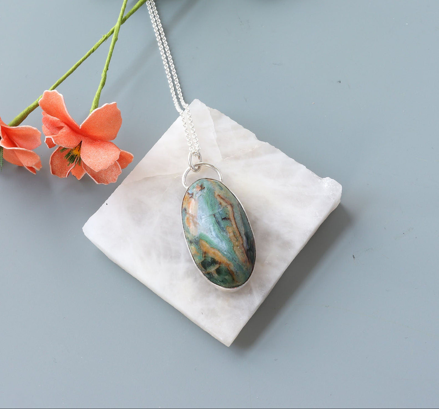 Necklace with Sonoran Jasper turquoise and desert rust hues pendant on a white square stone prop against a light blue background