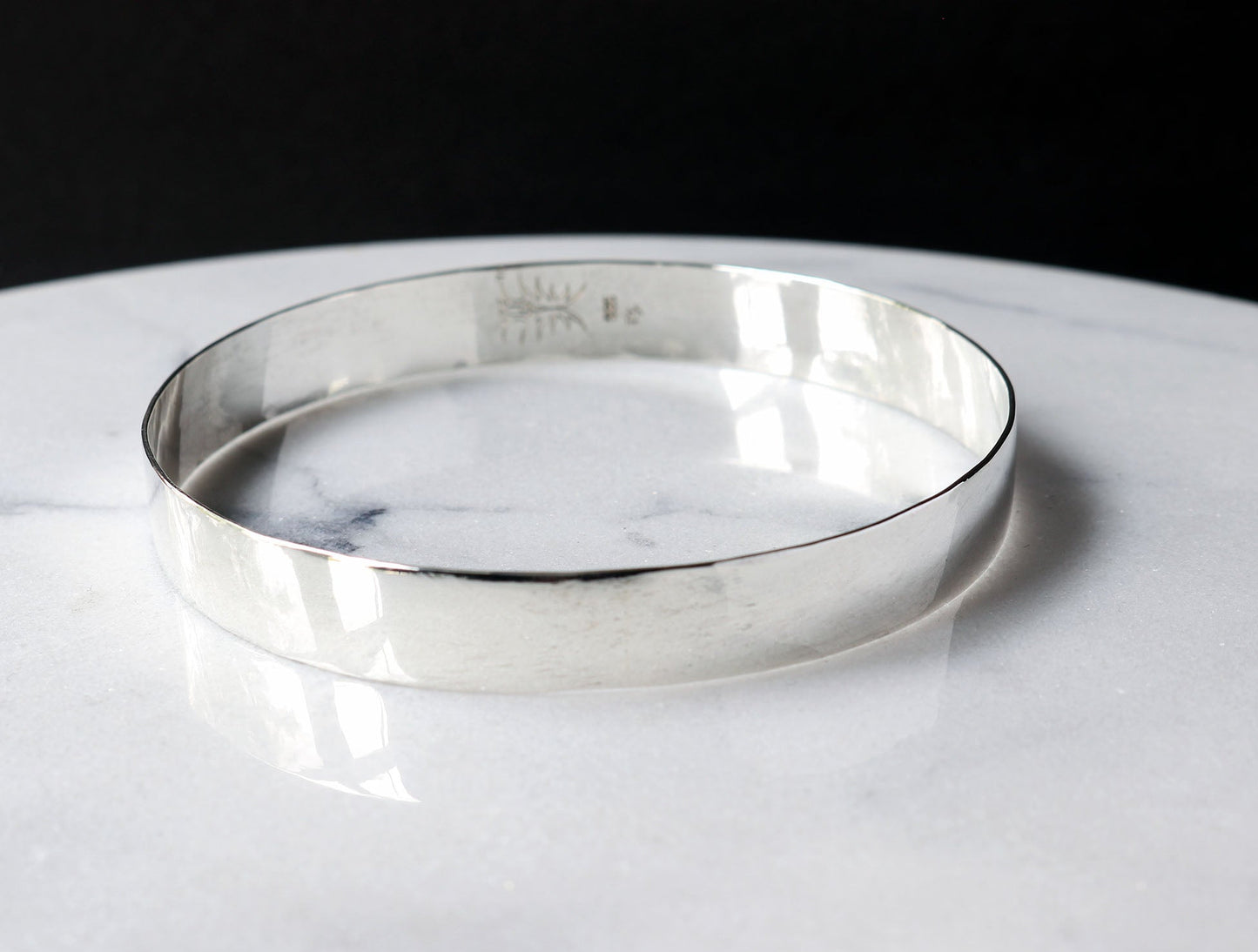 Front view of this solid Argentium Silver Beveled bangle bracelet.  Shown on white marble with black background.
