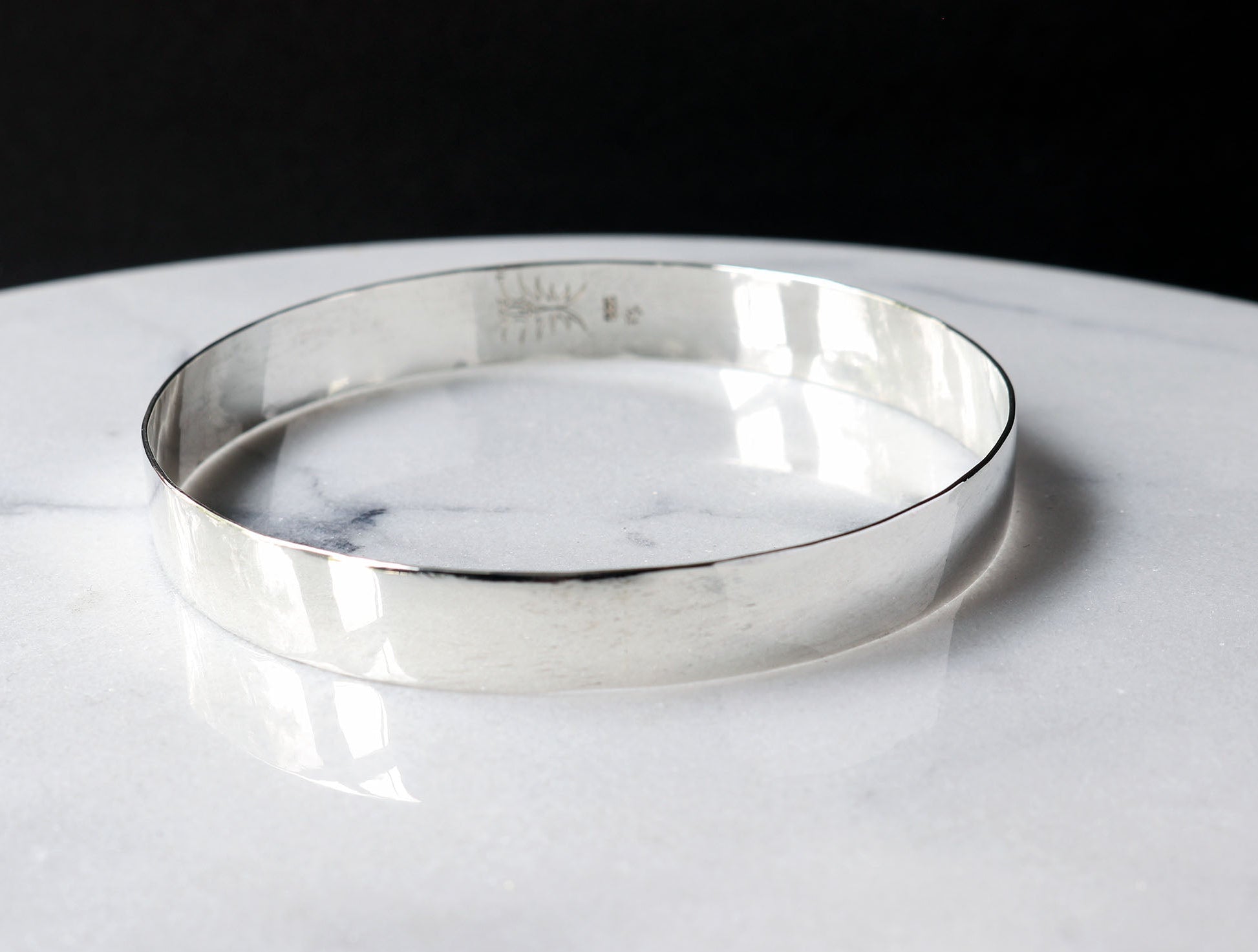 Front view of this solid Argentium Silver Beveled bangle bracelet.  Shown on white marble with black background.