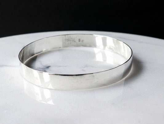 Front view of this solid Argentium Silver Beveled bangle bracelet.  Shown on white marble with black background.