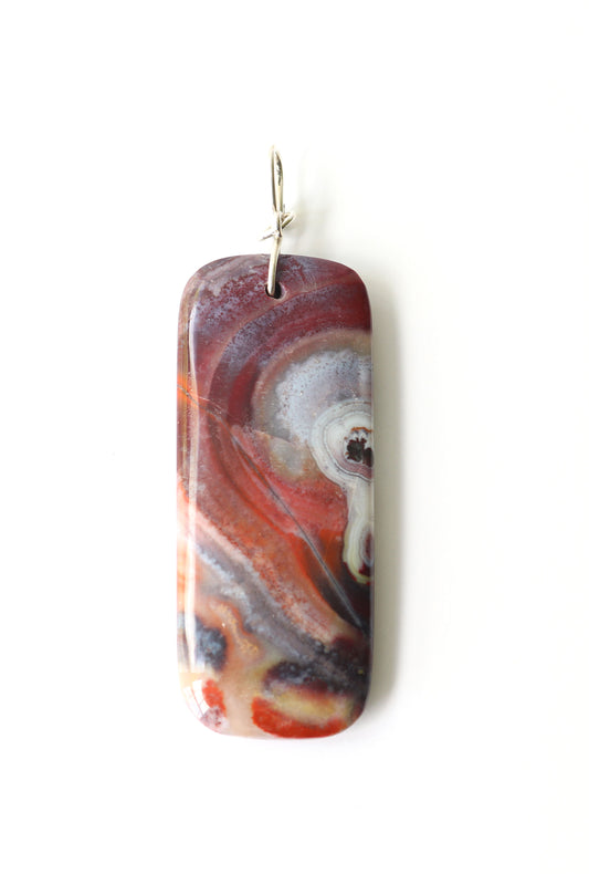 The front side of this one-of-a-kind handcut and polished Red Mexico Agate (Natural Banded Agate) Pendant features flowing bands of deep red, purple, orange, black, and white. Shown on white background. Argentium Silver custom wire bail.