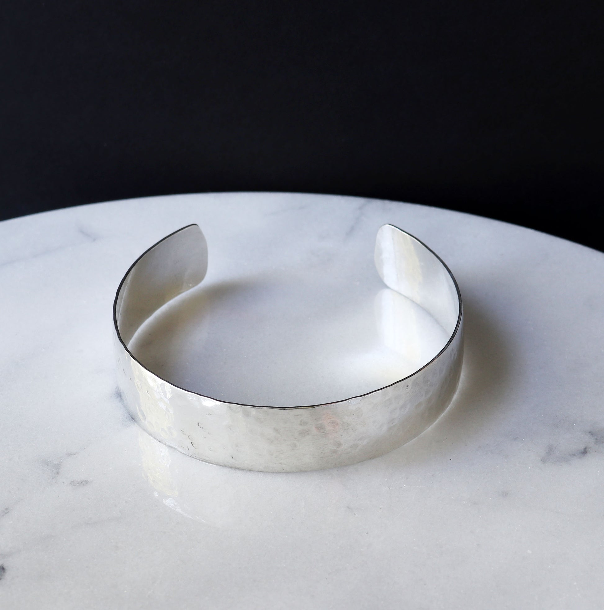 Argentiu, Silver hammered bracelet on a marble surface with a dark background